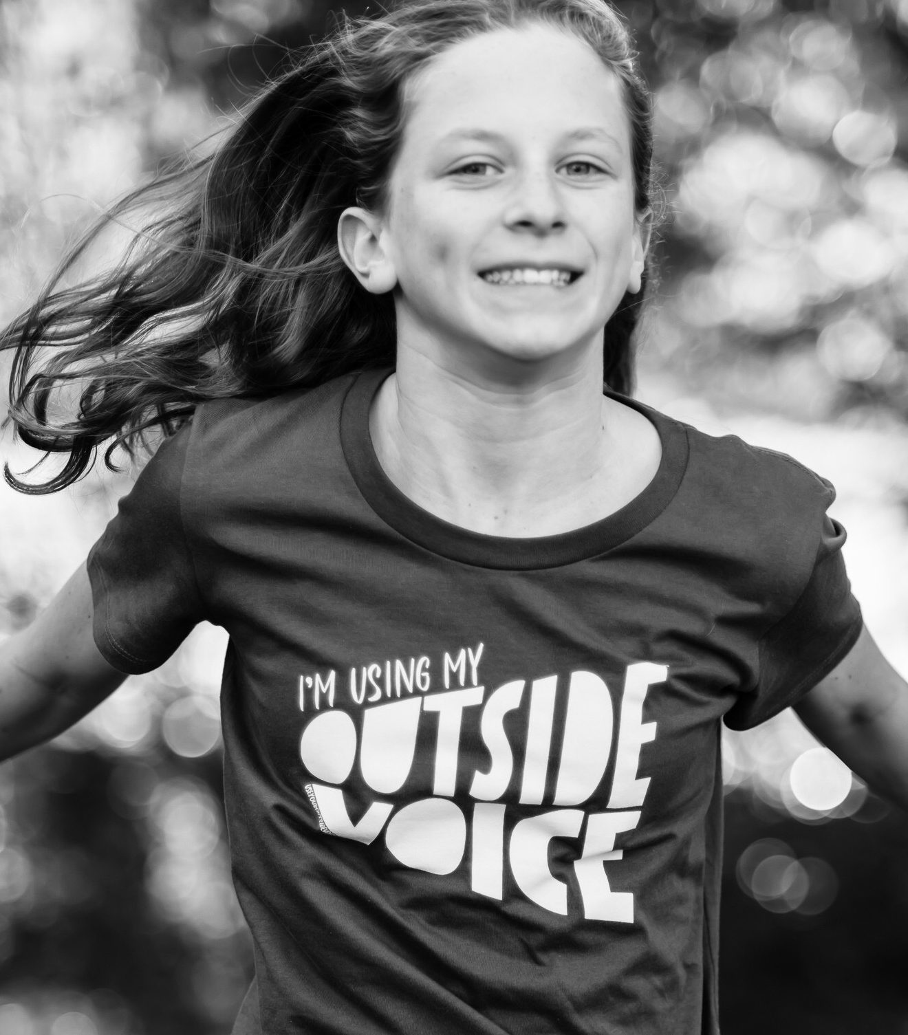 Black and white image of a blonde haired girl wearing a t-shirt with a logo that says, "I'm using my outside voice"